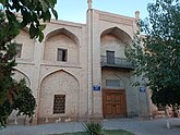 Early morning photo of a portion of the madrasa's cream-colored brick exterior, with light blue sky above