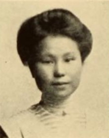 A young Japanese woman, hair in a bouffant updo, wearing a high-collared light-colored dress