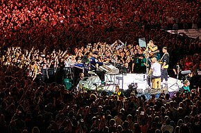 Coldplay stand on a stage surrounded by a large crowd of fans