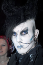 Goth im Grufti-Look, mit toupierten Haaren, Piercings, Rosenkranz und astropsychologischem Symbol auf der Stirn
