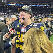 A football player talking to microphones on a football field.