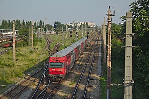 Red train with gray top on the middle track of a three-tracked main line