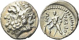 Drachme van Gortys, geslagen circa 98-94 v.Chr., zilver, diameter 17 mm, gewicht 3,14 g. De voorzijde toont het diadeemdragende hoofd van Zeus naar links, symbool van kracht en goddelijkheid in de Griekse wereld. Op de keerzijde staat een krijger afgebeeld, staand naar links, met een schild en speer, een verwijzing naar de militaire cultuur van de stadstaat Gortys. De inscriptie "ΓΟΡΤΙΝΙΩΝ" verwijst naar de stad zelf.