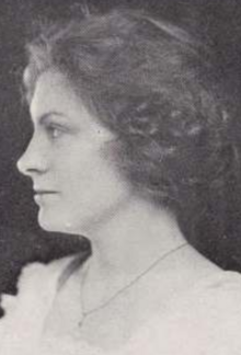 A young white woman in profile, with bobbed hair, wearing a blouse with a scooped neckline and a pendant on a chain