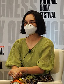 Little Badger is sitting in a chair in front of a backdrop for the 2022 National Book Festival