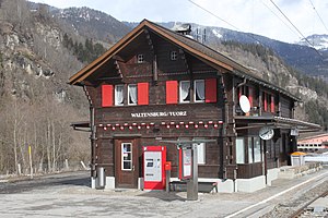 Two-story wooden building with gabled roof next to double-track railway line