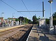 A set of two tram tracks between two platforms with shelters. There are houses in the background on the left.