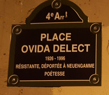 Auf dem Foto ist an einer sandsteinfarbenen Wand eine dunkelbraune Tafel mit goldfarbenen Buchstaben befestigt. Dort steht auf Französisch: Viertes Arrondissement. Place Ovida Delect (1926–1996). Widerstandskämpferin, nach Neuengamme Deportierte, Dichterin.