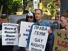 A group of people protest by holding up different signs; Peter Tatchell holds a bilingual Russian–English sign reading "GAY RIGHTS", "Outrage!"