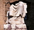 Fragment der Statue, die zentriert auf dem Podium aufgestellt ist