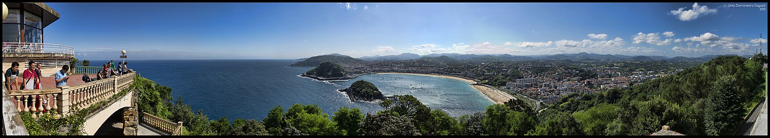 A city next to the blue sea, saw from a mountain. There is a bay with two urban beaches.