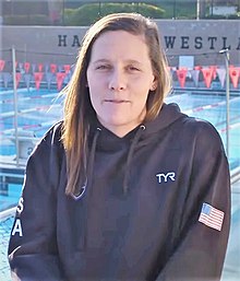 Alys Williams trägt die dunkelblaue Trainingsjacke des Nationalteams. Sie steht vor einem Freiluft-Schwimmbecken.