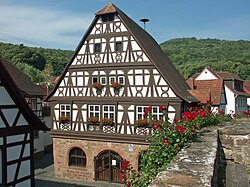 Prächtiger Fachwerkbau, massives Hallenerdgeschoss[1] aus Quadermauerwerk mit Rundbogenfenstern.