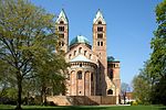 Looking toward the choir of a brick Romanesque cathedral. The twin bell towers, the transept crossing dome, and the roof are green copper.