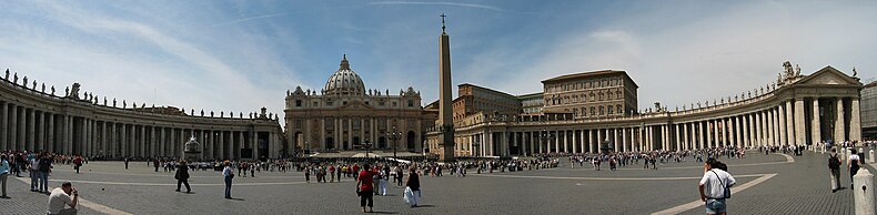 Panorama showing the facade of St Peter's at the centre with the arms of Berninis colonnade sweeping out on either side. It is midday and tourists are walking and taking photographs.