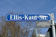 Großaufnahme des blauen Straßenschildes mit weißer Schrift Ellis-Kaut-Straße. Unter dem eigentlichen Straßenschild ist ein kleines graues Schild mit der Erklärung (wieder in weißer Schrift): Ellis Kaut (1920–2015), Schriftstellerin, Hörspielsprecherin, Erfinderin und Autorin der Kinderserie „Pumuckl“