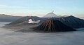 Das Tengger Massiv in Java (Indonesien) bei Sonnenaufgang. Im Bild die Vulkane Bromo (großer, rauchender Krater) und Semeru (rauchender Berg im Hintergrund). Der morgednliche Nebel umgibt die Spitzen, welcher auch ein Feld feinster Vulkanasche bedeckt.
