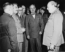 Three men in suits standing with several men in the background
