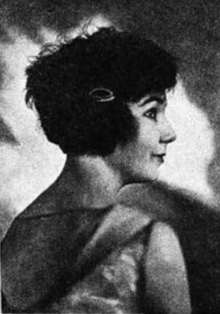 A young woman with light skin and dark hair cut in a short bob, photographed in profile, with her upper back facing the camera