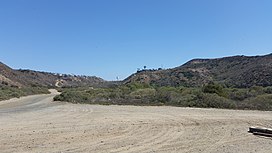 A valley, with schrub vegetation, a border barrier and highway in the distance