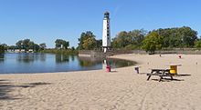 Beach with picnic table and several large wooden spools as tables; lighthouse in background with "Linoma" painted down side