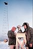 A man wearing a parka takes measurements with a theodolite in a frozen environment.
