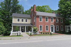 Photograph of a brick building with a modern addition on the left and a white picket fence.