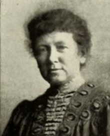 A white woman with her hair dressed back to the nape, wearing a dress or blouse with a distinctive ruffled and embroidered front