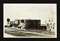 Unpaved road in front of businesses with a water tower in the background in 1910.