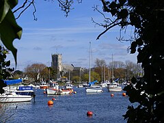 Looking across river with boats on we can see the priory against a bright blue sky