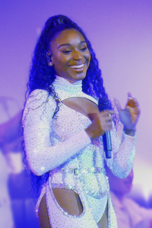 Normani hands a microphone in her hand, looking right and smiling