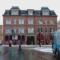 The front facade of the 4-storey Saint John City Market. It is made of red brick, with lines of beige stonework wrapping around the building framing the tall, arched windows. There is an large entryway in the centre of the bottom floor, with "CITY MARKET" in an arc of white letters above it.