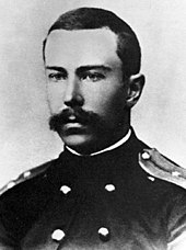 A teenage man with a full but neatly trimmed moustache, wearing a dark naval uniform