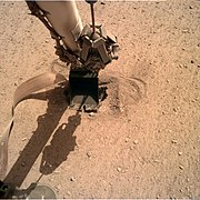 HP3 mole at the surface of Mars, with the lander scoop pressing on its back cap.