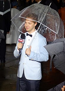 Devon Soltendieck in a suit, holding a microphone and umbrella