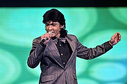 Jamal Abdillah singing onstage, wearing a black shirt and grey blazer and matching bowtie