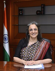 Madhabi Puri Buch sitting in front of the Indian flag, with her hands on a table