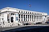 A white stone, classically designed, 4 story building. Doors are located at the corners of the building, on the second story with a grand staircase up to it, and are flanked by two ionic columns.