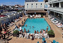 Photo of a swimming pool on a sunny day, with many people in and around the water