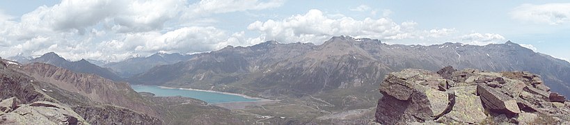 L’altipiano del Moncenisio con il suo lago visto dalla cresta del Monte Giusalet (3312 m) sopra il Rifugio Piero Vacca (2675 m) nell’estate del 2015. Sono visibili (da sinistra verso destra) la Punta Clairy (3162 m), il Passo de la Beccia (2717 m) e la Cima du Laro (2881m). Queste montagne sono parte Gruppo d'Ambin nelle Alpi Cozie. Dopo queste montagne si notano il Colle del Moncenisio (2081 m), che divide le Alpi Cozie dalle Graie (dietro questo, sotto le nuvole, il Massiccio della Vanoise che costituisce un supergruppo alpino a sé stante e che sovrasta la Moriana), l'Ouillon des Arcellins (2665 m), la Sommet de la Nunda(3025 m), il Col du Lou (3024 m), Signal du Grand Mont Cenis (3377 m), Punta Roncia (3612m), la Pointe du Vieux (3464m), la Pointe de la Haie (3452m), la Punta Lamet (3504m), Roche Michel (3429), I Tre Denti (3281–3285 m), tutte montagne del Gruppo Roncia-Lamet, poi la Punta Marmottere (3387 m), il Passo della Novalesa, il Rocciamelone (3537 m), montagne del Gruppo del Rocciamelone, parte insieme al Roncia-Lamet della Catena Rocciamelone-Charbonnel nelle Alpi Graie. Sotto la Punta Lamet si scorge il luogo dove sorgeva la Batteria Paradiso e dove sono ancora presenti i ruderi della Batteria La Court. Si nota anche la Strada statale 25 del Moncenisio.