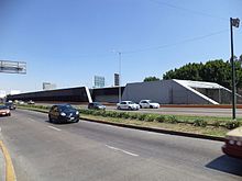 Picture of the station in the middle of Río Consolado Avenue. Several automobiles surround the station.