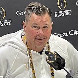 A football coach sitting in front of a microphone.