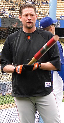 A man in a black baseball uniform pointing a bat towards the camers