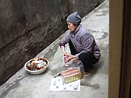 Woman burning joss papers in front of her house in Hanoi after having offered food to her ancestors