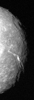 The right half of a round spherical body that is illuminated. The terminator runs along the right edge. A large crater with a central pit can be seen at the terminator in the upper half of the image. A large canyon runs from the darkness at the lower-right side to visible center of the body.