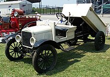 Pick up truck built circa 1918, painted in white, with a rear-end cargo box that lifts up to dump its content