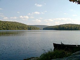 A lake stretches midway across the image to its far shore, covered in green trees. Above, a lightly cloudy blue sky.