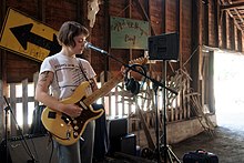 Kenney playing guitar in front of a microphone