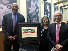 A photo of Williams standing next to the framed University of Washington School of Social Work 2013 Distinguished Alumnus Award on an easel. One the other side of the easel is Edwina Uehara and Richard Catalano Jr.