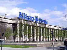 Auf dem Dach des Hauses steht zeitweilig das große blaue Logo „Allianz [Logo] Arena“, das ansonsten am Münchner Fußballstadion hängt